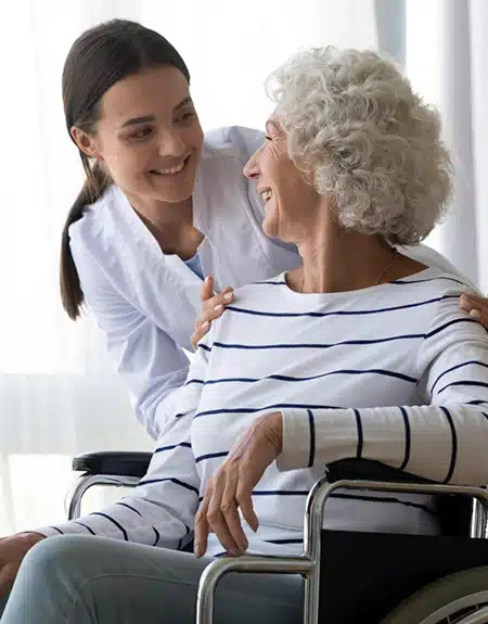 A caregiver smiles at an older woman in a wheelchair. | Senior Care